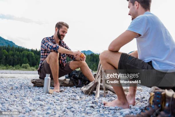 germany, bavaria, two hikers having a rest at camp fire on gravel bank - barefoot men stock-fotos und bilder