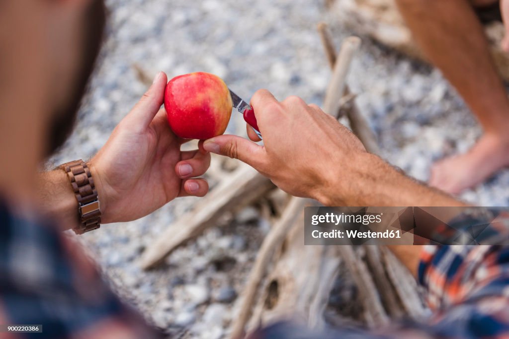 Man's hand cutting apple at camp fire