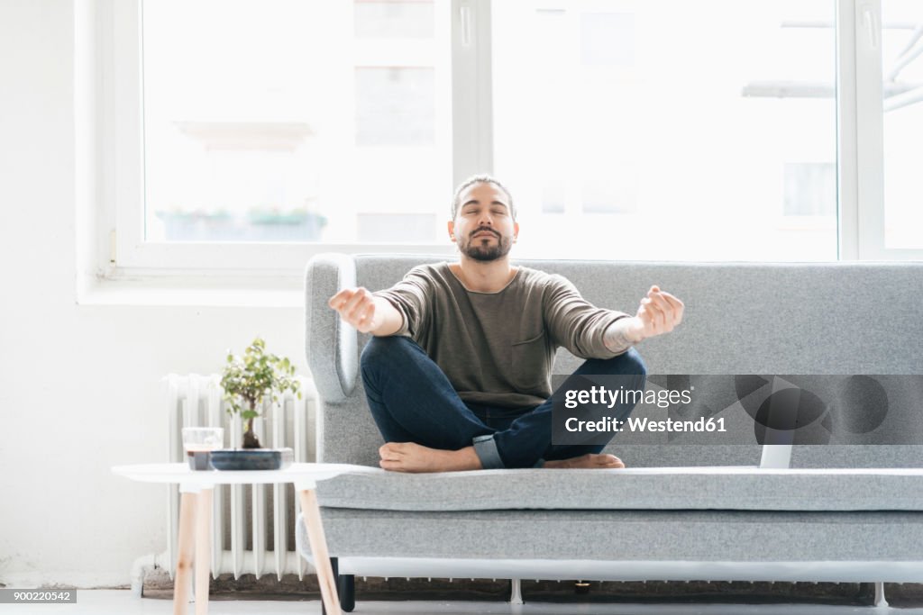 Portrait of man with eyes closed sitting on the couch doing yoga exercise