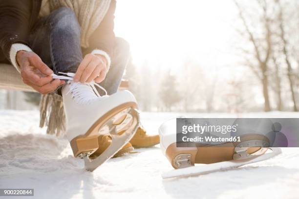woman sitting on bench in winter landscape putting on ice skates - eislaufen stock-fotos und bilder