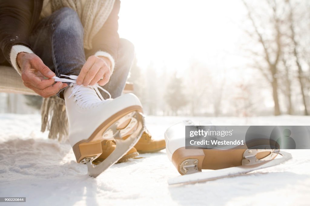 Woman sitting on bench in winter landscape putting on ice skates