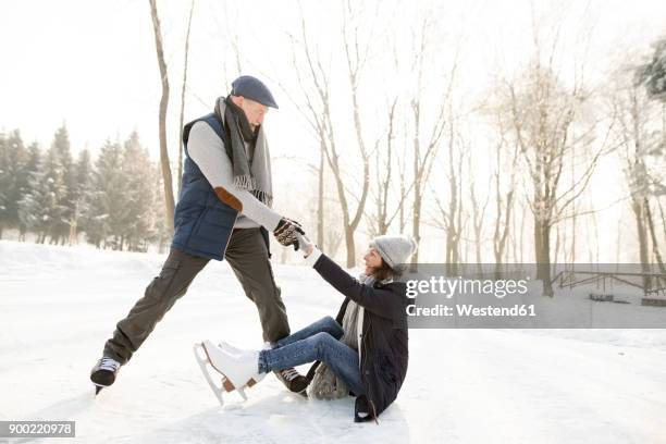 man helping ice skating woman getting up from frozen lake - learning to ice skate stock pictures, royalty-free photos & images