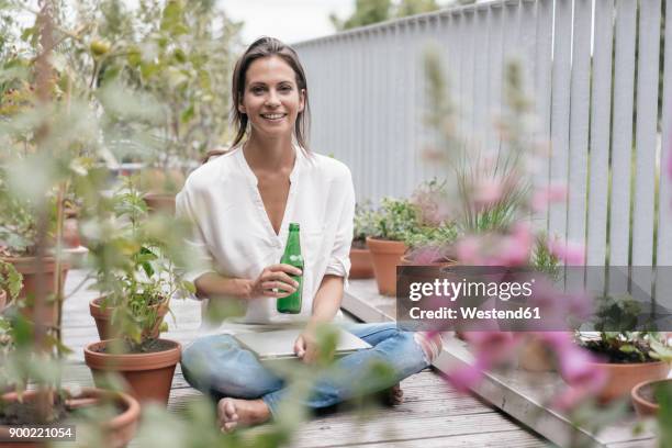 smiling woman with bottle and laptop relaxing on balcony - bottle water stock-fotos und bilder