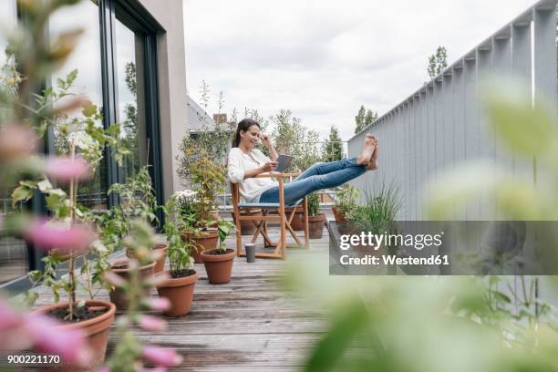 smiling woman relaxing on balcony using tablet - balcony stock-fotos und bilder