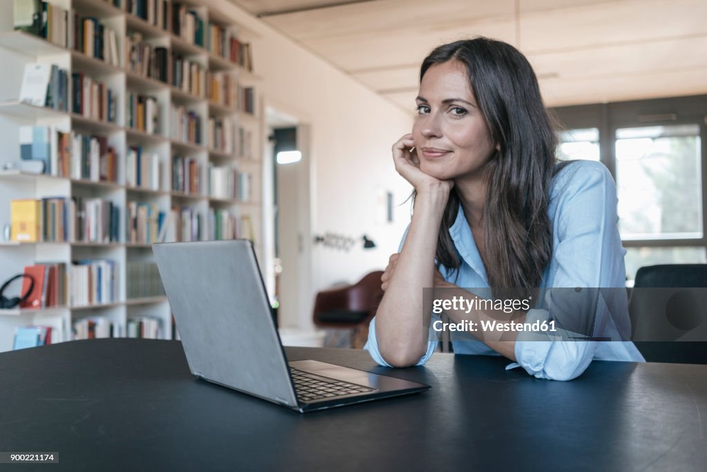 Portrait of smiling woman sitting at table with laptop