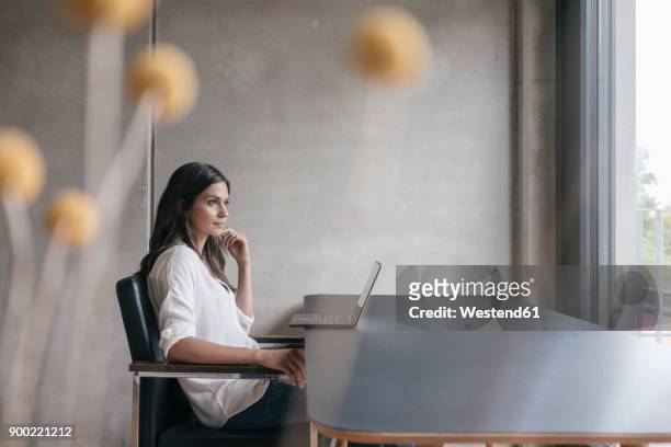 thoughtful woman sitting at table with laptop - business woman side stockfoto's en -beelden