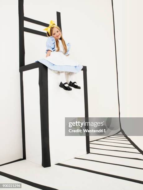 smiling little girl dressed up as alice in wonderland sitting on oversized chair - alice franco foto e immagini stock