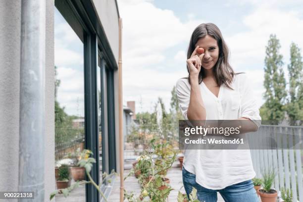 portrait of smiling woman on balcony holding tomato - tomato harvest stock-fotos und bilder