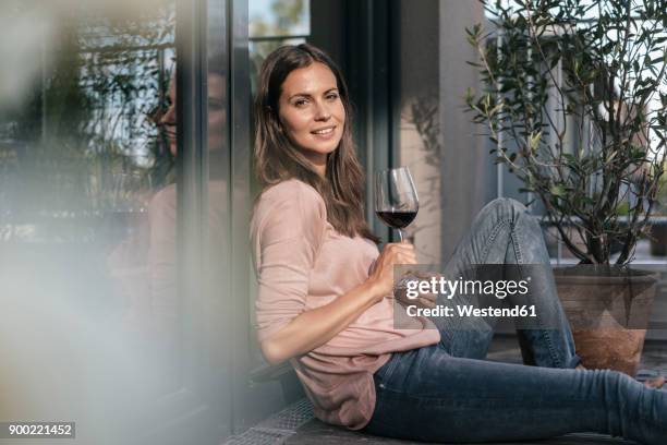 woman with glass of red wine relaxing on balcony - brown hair drink wine stock-fotos und bilder