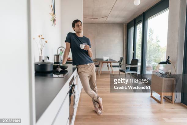 young man holding cup of coffee in kitchen at home - kitchen stock-fotos und bilder