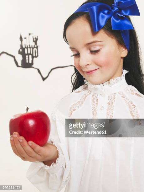 portrait of little girl dressed up as snow white looking at red apple - schneewittchen stock-fotos und bilder