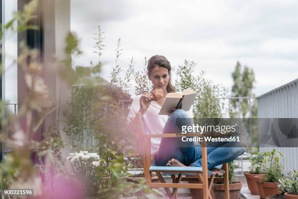 woman eating croissant and reading book on balcony - balcony stock-fotos und bilder