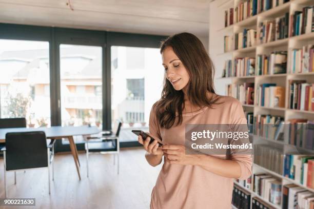 smiling woman looking at cell phone at home - bel appartement stockfoto's en -beelden