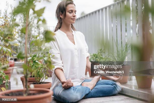 woman sitting on balcony practicing yoga - mindfulness stock-fotos und bilder