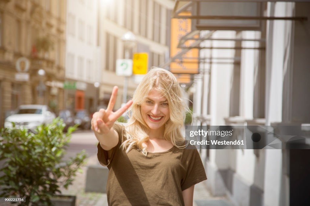 Portrait of happy blond woman showing victory sign