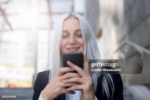 smiling young businesswoman checking cell phone in the city - woman silver hair young ストックフォトと画像