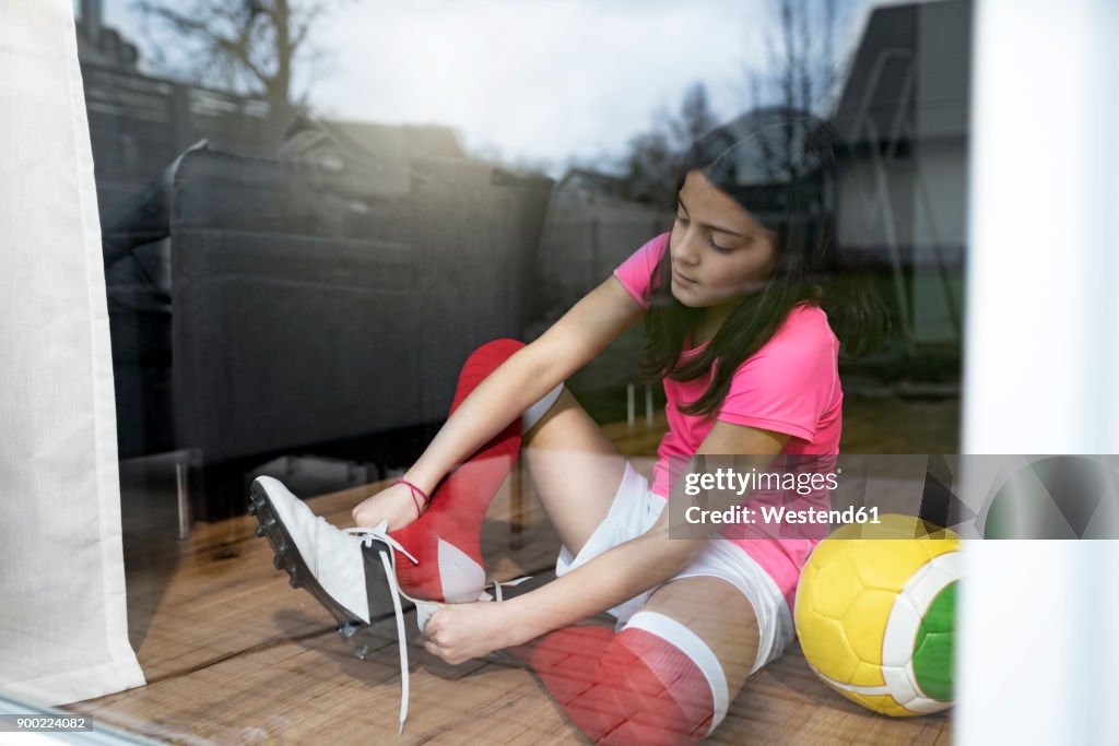 Girl putting on soccer shoes in front of living room window