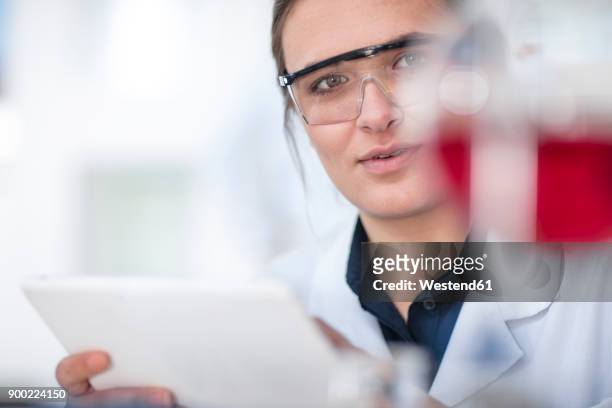 scientist working in lab holding a tablet looking at flask - lab closeups stock-fotos und bilder