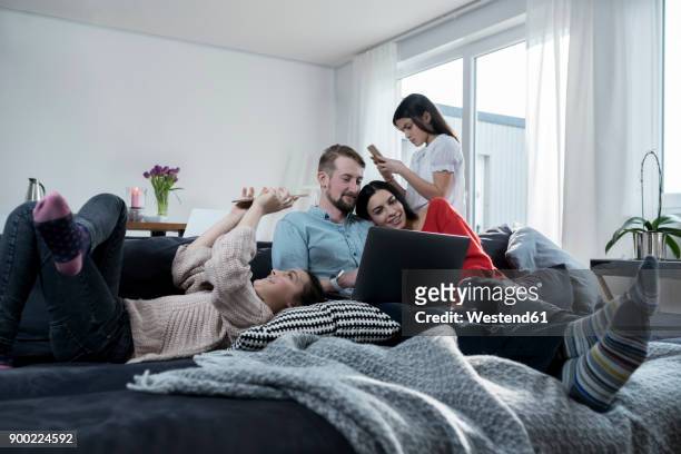 parents and twin daughters on sofa using portable devices - familie online stock pictures, royalty-free photos & images