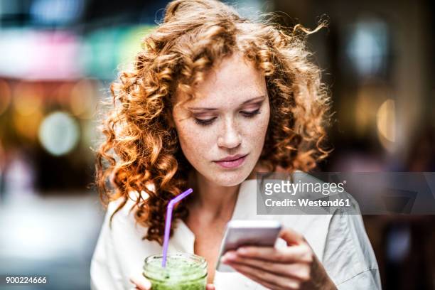 portrait of young woman with beverage looking at cell phone - smartphone cuisine stock-fotos und bilder