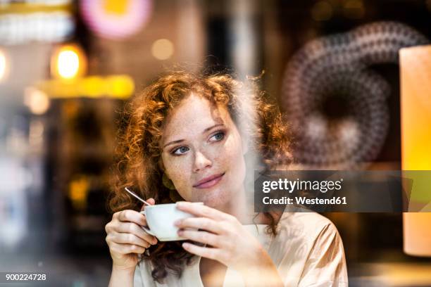 portrait of smiling young woman with coffee cup behind windowpane of a coffee shop - drinking coffee stock-fotos und bilder