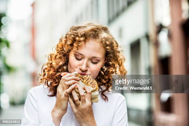 portrait of young woman eating bagel outdoors - eating bread stockfoto's en -beelden
