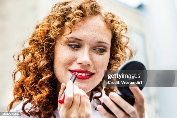 portrait of freckled young woman applying lipstick - lipstick fotografías e imágenes de stock