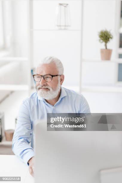 smiling mature man with beard and glasses at desk - person surrounded by computer screens stock pictures, royalty-free photos & images