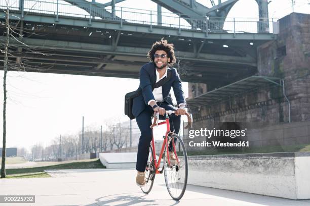 smiling businessman riding bicycle at riverside bridge - velofahren stock-fotos und bilder
