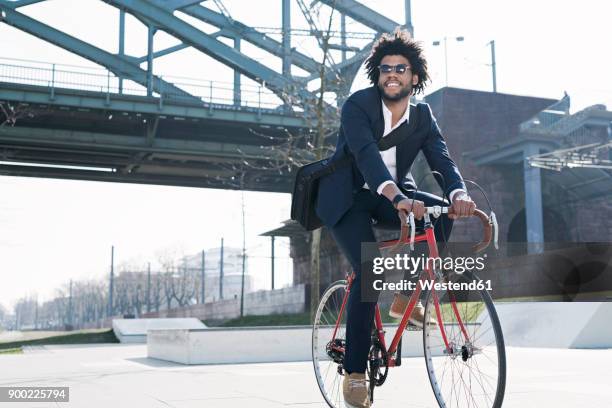 smiling businessman riding bicycle at riverside bridge - business man on bike stock-fotos und bilder