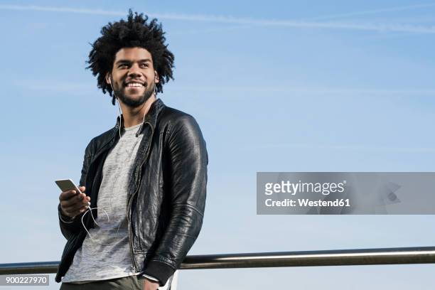 smiling man with earphones listening to music on his smartphone - afro man stock pictures, royalty-free photos & images