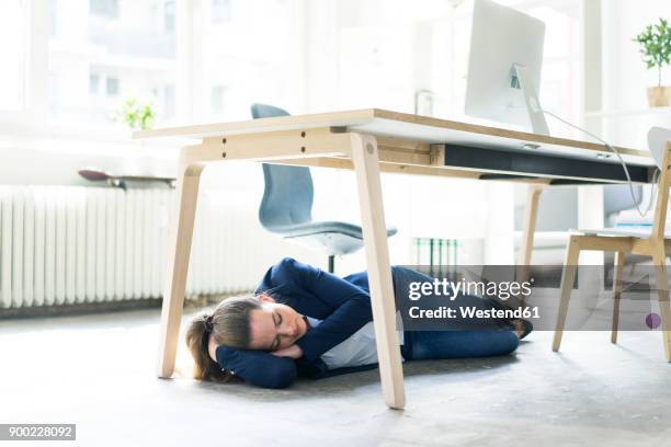 businesswoman lying under the table in office sleeping - businesswoman under stock-fotos und bilder