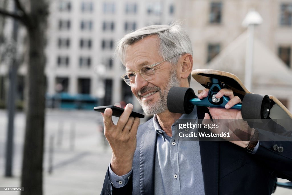 Grey-haired businessman with longboard and smartphone