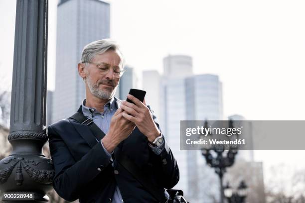 grey-haired businessman looking at smartphone standing next to street lamp - hesse stock-fotos und bilder