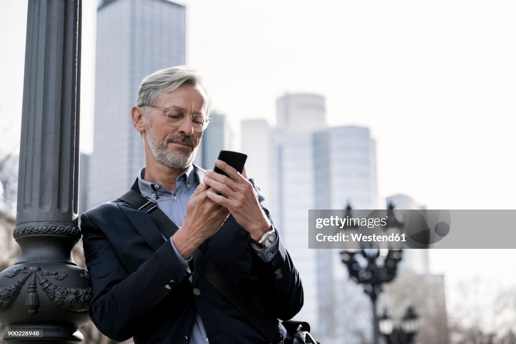 Grey-haired businessman looking at smartphone standing next to street lamp