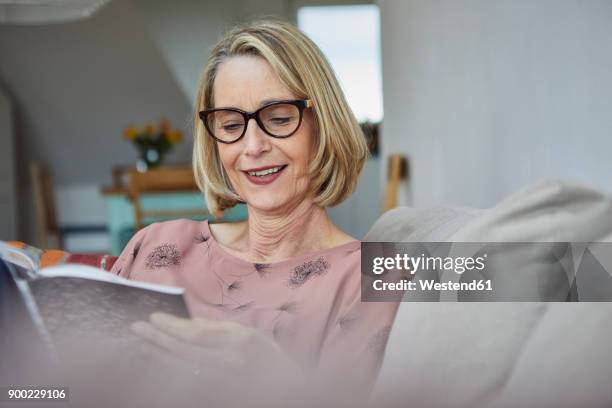 smiling mature woman at home on the sofa reading a book - caitlyn jenner signs copies of her new book the secrets of my life stockfoto's en -beelden