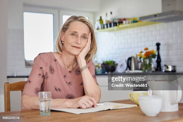 portrait of mature woman with notebook at kitchen table - 50s woman writing at table imagens e fotografias de stock