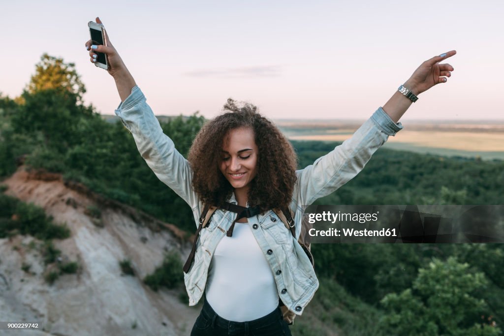 Happy teenage girl with smartphone and backpack in nature