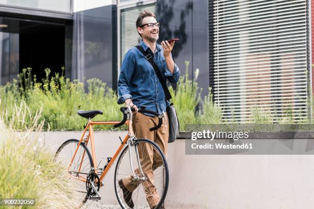 smiling businessman with cell phone pushing bicycle - velo stock-fotos und bilder