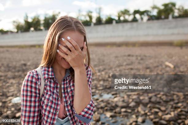 happy young woman covering her face on stony beach - hand covering face stock pictures, royalty-free photos & images