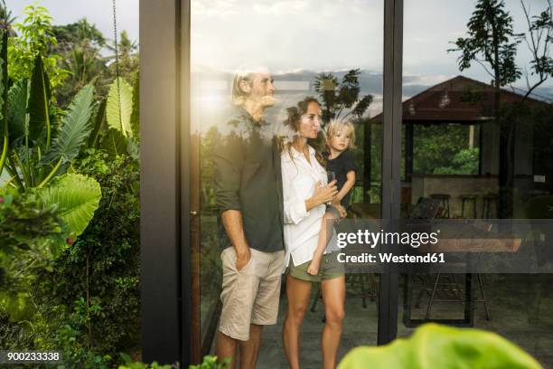 garden view of parents with their young son looking outside of their design house surrounded by lush tropical garden - family home exterior stock-fotos und bilder