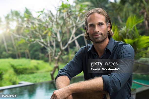 portrait of handsome man in front of swimming pool and stunning tropical garden - lush stock pictures, royalty-free photos & images