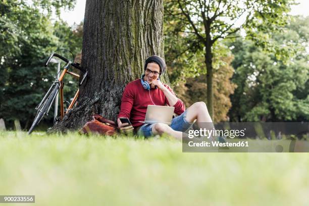 man using laptop and cell phone in park - le cap - fotografias e filmes do acervo