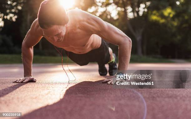 shirtless man exercing push ups on sport field - push ups stock-fotos und bilder