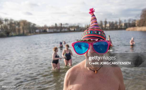 Man poses with giant plastic glasses after taking part in the traditional New Year swimm in the Orankesee lake in Berlin on January 1, 2018. / AFP...