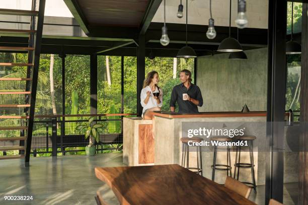 couple having breakfast and smiling at each other in modern design kitchen with glass facade surrounded by lush tropical garden - kitchen coffee home stock-fotos und bilder