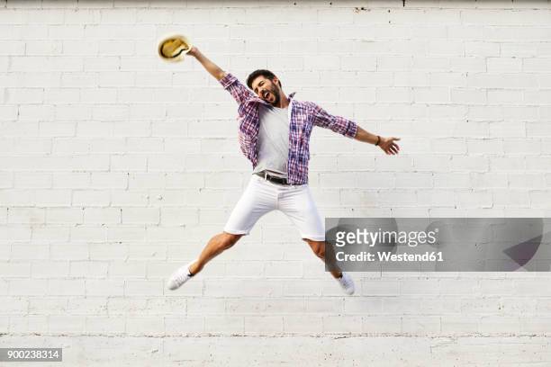 happy man jumping mid-air in front of white wall - white shorts stock-fotos und bilder