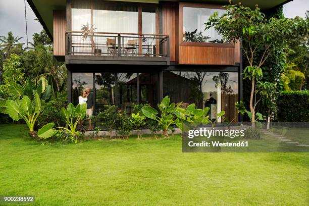 garden view of couple standing in modern design house surrounded by lush tropical garden - lush grass stock pictures, royalty-free photos & images