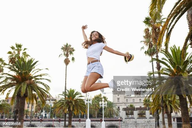 spain, barcelona, happy woman jumping mid-air surrounded by palm trees - hot pants ストックフォトと画像