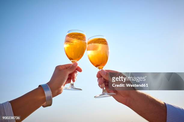 couple clinking spritz glasses before blue sky - hand glasses stockfoto's en -beelden